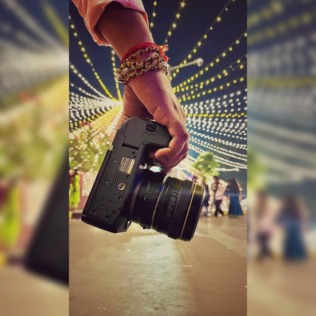 Cameraman hand holding Canon DSLR with lens, wearing rudraksha bracelet